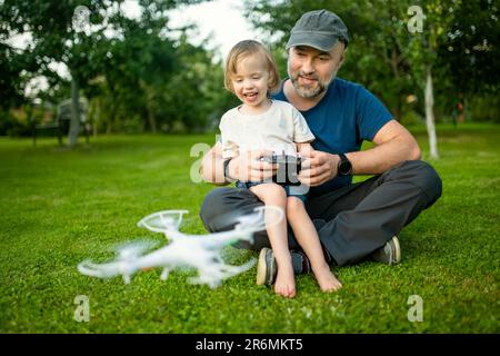 Vater und Sohn beobachten und steuern eine Drohne. Netter kleiner Junge, der seinem Vater hilft, eine Drohne per Fernbedienung zu bedienen. Familienurlaub. Stockfoto