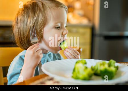 Niedlicher kleiner Kleinkind Junge, der Brokkoli isst. Erste feste Lebensmittel. Frisches Bio-Gemüse für Kleinkinder. Gesunde Ernährung für Familien mit Kindern. Stockfoto