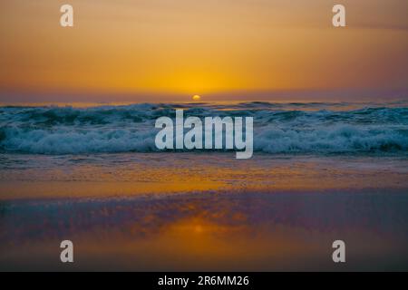 Ein atemberaubender orangefarbener Sonnenuntergang, der sich vom blauen Ozean reflektiert Stockfoto