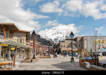 Banff, Alberta, Kanada - 15. 2023. April; Village, Township im Frühling mit schneebedeckten Bergen im Hintergrund und Touristen auf den Straßen, S. Stockfoto