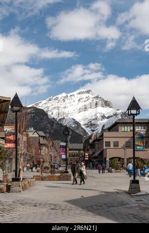 Banff, Alberta, Kanada - 15. 2023. April; Village, Township im Frühling mit schneebedeckten Bergen im Hintergrund und Touristen auf den Straßen, S. Stockfoto