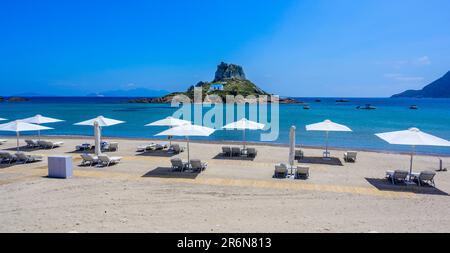 Liegestuhl und Sonnenschirm am wunderschönen Strand Agios Stefanos vor der Paradiesinsel Kastri - historische Ruinen und Paradieslandschaft an der Küste der Insel Stockfoto