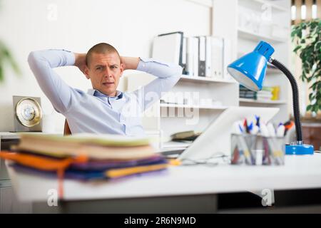 Schockierter Geschäftsmann, der mit vielen Papiermappen am Bürotisch saß Stockfoto