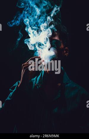 Schwarzer junger Mann mit Brille, Zigarre mit Nebel im schwarzen Hintergrund, dezentes Licht. Stockfoto