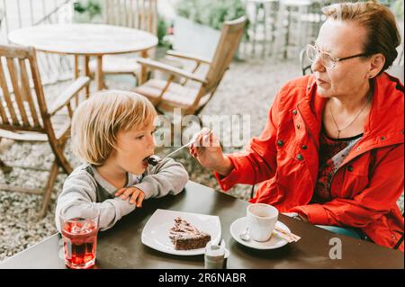 Großmutter und kleiner Junge verbringen Zeit zusammen in einem Café im Freien, essen Schokoladenkuchen, Familienbeziehungen Stockfoto