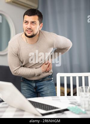 Der Mensch erleidet starke Schmerzen in seiner Seite, die Frucht der langen Arbeit mit einem Notebook zu Hause Stockfoto