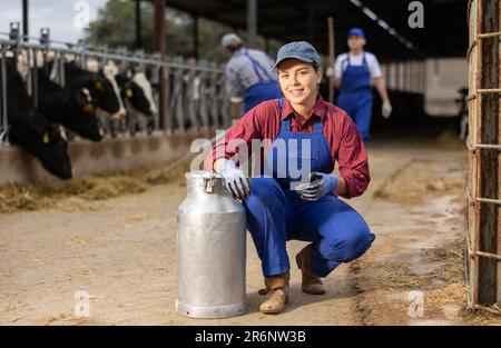 Junglandwirte mit positivem Befund, die während der Arbeit im Milchbetrieb in der Nähe des Stalls mit Kühen Milchkräuter befördert Stockfoto