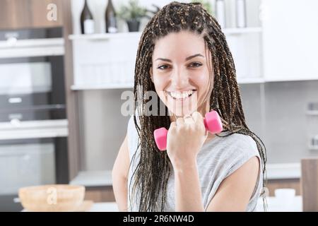 In ihrem eigenen Zuhause demonstriert eine junge Frau mit Boxgeflechten ihren sportlichen und sportlichen Lebensstil, da sie Zeit und Platz für das Training mit kleinen Gewichten aufwendet. T Stockfoto