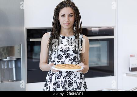 Begeisterter Koch ist zufrieden in ihrer hellen Küche. Sie bereitet ein Essen zu und trägt dafür ein elegantes schwarz-weißes Kleid. Feld b Stockfoto