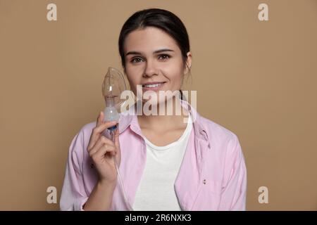 Glückliche junge Frau mit Vernebler auf dunkelbeigem Hintergrund Stockfoto