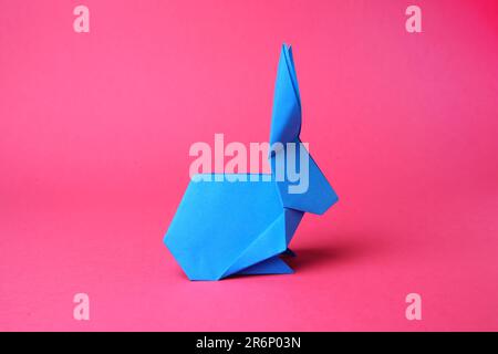 Hellblauer Papierhasen auf pinkfarbenem Hintergrund. Origami-Kunst Stockfoto