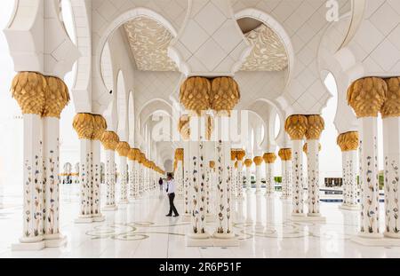 Die Menschen gehen zwischen den Säulen und Bögen der Scheich-Zayid-Moschee, Abu Dhabi VAE Stockfoto