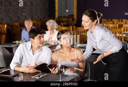 Die Kellnerin nimmt die Bestellung von einem jungen Paar im Restaurant entgegen Stockfoto