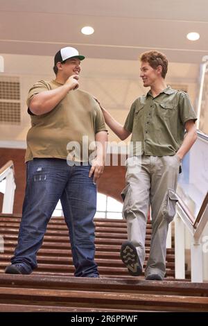 Schüler, Freunde von Teenagern und Jungen, die mit einem Lächeln die Uni- und Schultreppe hinuntergehen. Gespräch, Gespräch und Diskussion über Männergruppen-Feeing Stockfoto