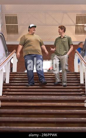 Schüler, Teenager und Campus-Jungs gehen mit einem Lächeln die Stufen zur Universität und Schule hinunter. Gespräch, Gespräch und Diskussion über die Männergruppe Stockfoto