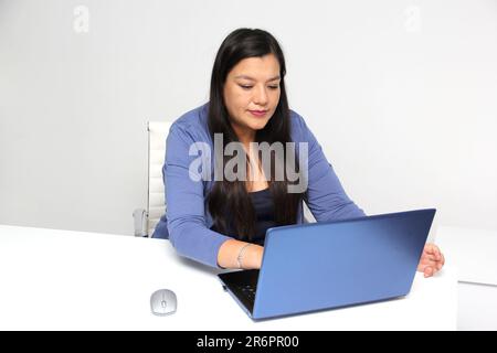 Die vierzigjährige Latina arbeitet in ihrem Büro mit ihrem Laptop und leidet unter Stress, der durch ihren Job verursacht wird, der zu einem Burn-out führt, geistig, physisch Stockfoto