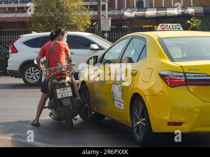 BANGKOK, THAILAND, 28 2023. JANUAR, Eine Frau auf einem Motorrad löst einen Zusammenstoß mit einem Taxifahrer an einer Kreuzung - Ein sich drehendes Taxiauto lief in ein Wom Stockfoto