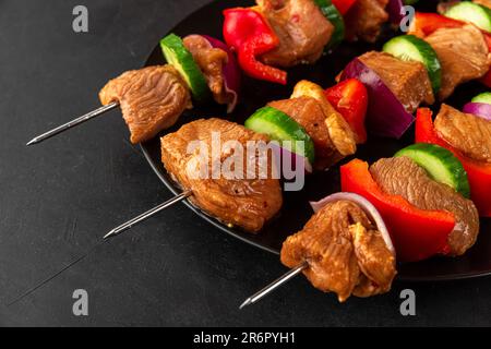 Nahaufnahme von Spießen mit rohem Fleisch. Mariniertes Schweinefleisch mit Gemüse und Gewürzen auf schwarzem Hintergrund Stockfoto