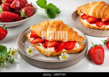 Croissants mit frischen Erdbeeren und Frischkäse auf einem Teller mit Blumen für ein leckeres Frühstück. Schließen Stockfoto