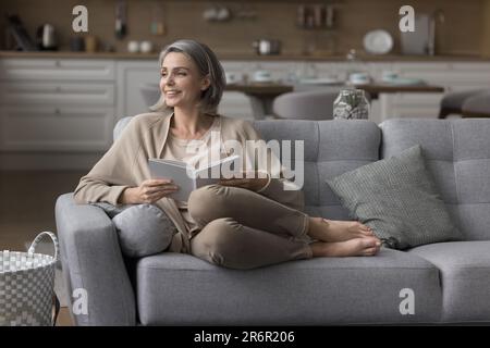 Fröhliche, grauhaarige Leserin, die sich zu Hause entspannt Stockfoto