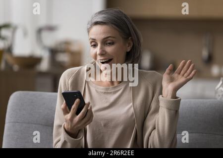 Eine freudige, überraschende, reife Frau, die ein Smartphone in der Hand hält und auf den Bildschirm schaut Stockfoto