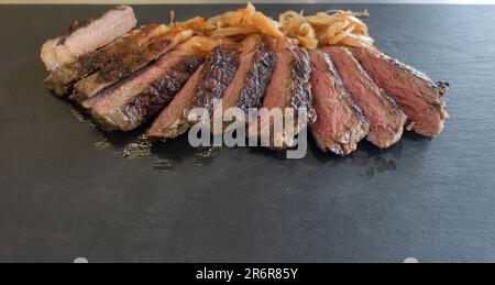 Erleben Sie die Harmonie der Geschmacksrichtungen, wenn das Filetsteak in dünne Scheiben geschnitten und mit karamellisierten Zwiebeln, kunstvoll präsentiert auf einem raffinierten Bla, ergänzt wird Stockfoto