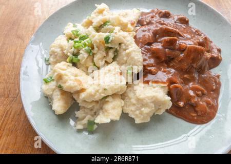 Tauchen Sie ein in unsere hausgemachten Knödel mit beruhigenden Aromen und Geschmäckern, gefüllt mit herzhaftem Rindereintopf und serviert auf einem köstlichen Teller. Stockfoto