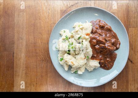 Genießen Sie hausgemachte Knödel, großzügig gefüllt mit saftigem Rindereintopf, elegant auf einem Teller präsentiert. Stockfoto