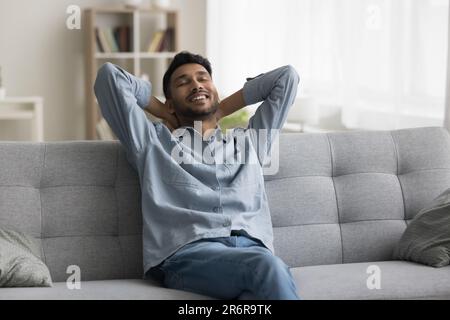 Positiver, entspannter junger Indianer, der auf dem Sofa sitzt Stockfoto
