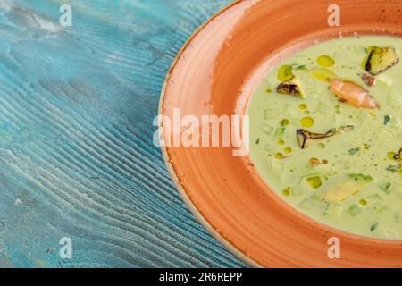 Cremige Avocado-Suppe mit Zucchini und Lachsfisch auf blauem Holzhintergrund. Speicherplatz kopieren Stockfoto