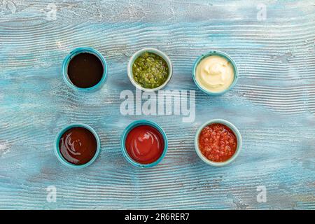 soja, Pesto, Mayonnaise, tkemali, Ketchup, Adjika-Saucen in Tonschüsseln auf blauem Holzhintergrund Stockfoto