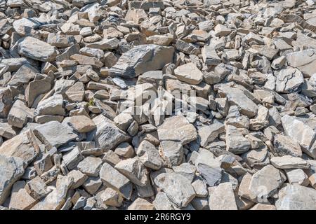 Feld aus gebrochenem Hardcore-Stein in hellem Sonnenlicht. Ich bin daran gewöhnt, verfallene Bauernhöfe zu flicken. Der größte Stein ist etwa 25cm. Auf steinigen Boden fallen Stockfoto