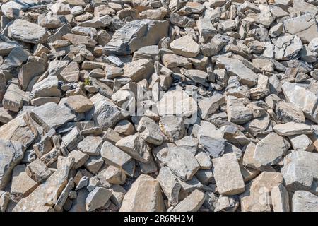 Feld aus gebrochenem Hardcore-Stein in hellem Sonnenlicht. Ich bin daran gewöhnt, verfallene Bauernhöfe zu flicken. Der größte Stein ist etwa 25cm. Auf steinigen Boden fallen Stockfoto