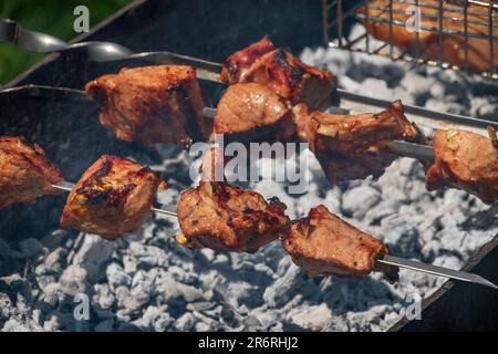 Stücke gegrilltes Fleisch auf den Spießen. Traditionelles Barbecue-Essen im Sommer. Shish Kebab auf dem Grill Stockfoto