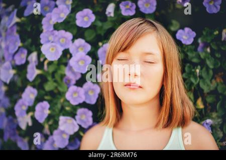 Tagträumendes hübsches Mädchen, Nahaufnahme Porträt gegen die lila Blumenwand. Augen zu Stockfoto