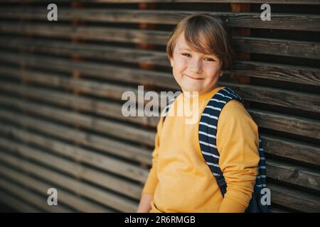 Außenporträt eines süßen Jungen mit gelbem Sweatshirt und Rucksack. Wieder-in-die-Schule-Konzept Stockfoto