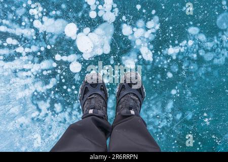 Mann in Stiefeln steht auf einem gefrorenen See mit natürlicher Blase im Winter in Kanada Stockfoto