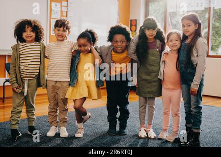 Eine Gruppe von Grundschülern steht zusammen in einem Klassenzimmer und schaut in die Kamera. Sie tragen legere Kleidung und freuen sich, in den nächsten Tagen wieder da zu sein Stockfoto