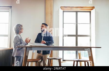 Zwei Geschäftsleute, die in einem Coworking-Bereich eine Diskussion führen. Geschäftskollegen sprechen, während sie zusammen stehen. Geschäftsleute arbeiten zusammen Stockfoto
