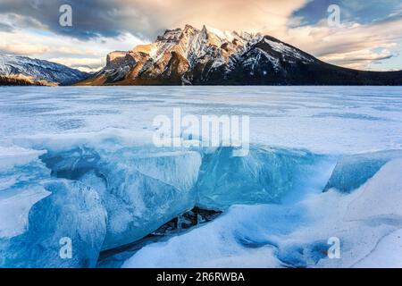 Schöner Blick auf den Frozen Lake Minnewanka mit felsigen Bergen und im Winter gerissenem Eis im Banff National Park, Alberta, Kanada Stockfoto