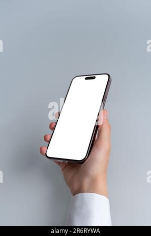 Halten Sie ein Smartphone mit einem leeren, isolierten Bildschirm vor grauem Hintergrund in der Hand. Isolierter Bildschirm für Modell-, App- oder Webseitenpräsentation Stockfoto