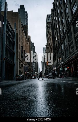 Ein Bild einer belebten Straße in einer städtischen Umgebung an einem regnerischen Tag, beleuchtet durch die Straßenlaternen und Neonlichter der nahegelegenen Unternehmen Stockfoto