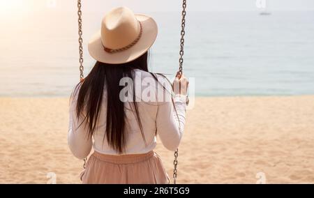 Foto einer nicht wiedererkennbaren Frau, die in einem Schaukelstuhl draußen am Strand sitzt. Stockfoto