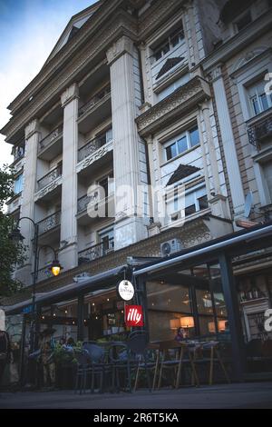 Ein Gebäude mit vielen Fenstern und alter Architektur und ein Restaurant im ersten Stock mit einer Straßenbeleuchtung davor, alles in einer düsteren Umgebung Stockfoto