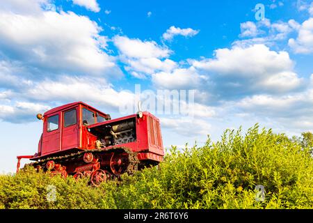 Der rote Traktor des alten Modells steht auf dem Feld. Traktor auf dem Feld. Traktor fährt im Gelände. Der alte sowjetische Traktor steht auf dem Feld. Stockfoto