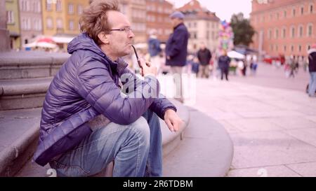 Warschau, Polen. 11. Juni 2023. Erwachsener Mann sitzt auf dem Platz und raucht eine Tabakpfeife auf dem Palastplatz, Warschauer Altstadt (Bild: © Andrey Nekrasov/ZUMA Press Wire) NUR REDAKTIONELLE VERWENDUNG! Nicht für den kommerziellen GEBRAUCH! Stockfoto