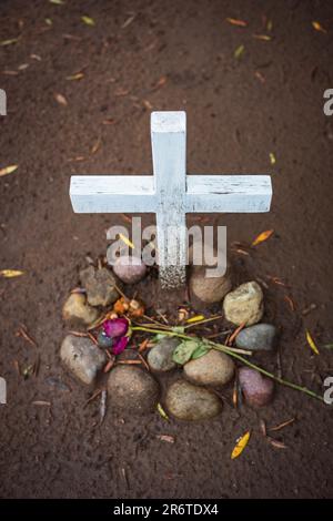 Ein unmarkiertes Grab, das auf einem Friedhof in San Diego, Kalifornien, gefunden wird, ist mit einer verwesenden Rose und einem weiß bemalten Holzkreuz ausgestellt. Stockfoto