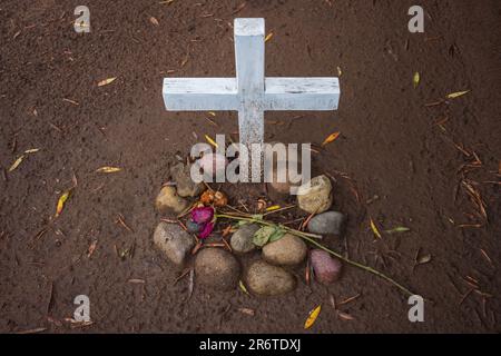 Ein unmarkiertes Grab, das auf einem Friedhof in San Diego, Kalifornien, gefunden wird, ist mit einer verwesenden Rose und einem weiß bemalten Holzkreuz ausgestellt. Stockfoto