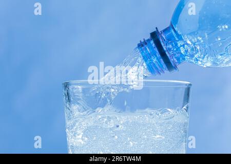 Aus dem Flaschenhals fließt frisches und kühles Wasser. Wasser wird aus einer Plastikflasche in ein Glas gegossen. Speicherplatz kopieren. Nahaufnahme Stockfoto