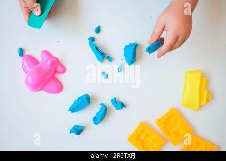 Die Hände eines kleinen Jungen spielen mit blauem Modelton auf weißem Hintergrund. Heimunterricht mit Ton. Draufsicht. Frühentwicklungskonzept Stockfoto